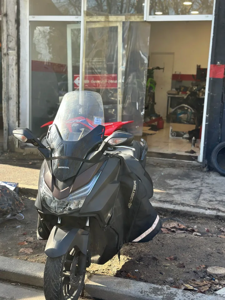 Scooter gris stationné devant l’entrée ouverte de l’atelier Mecabike.