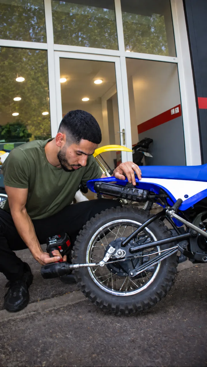 Un mécanicien intervient sur la roue arrière d’une moto bleue.